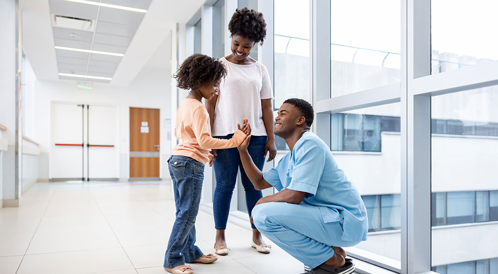 Picture of a Black family in a hospital hallway smiling at each other